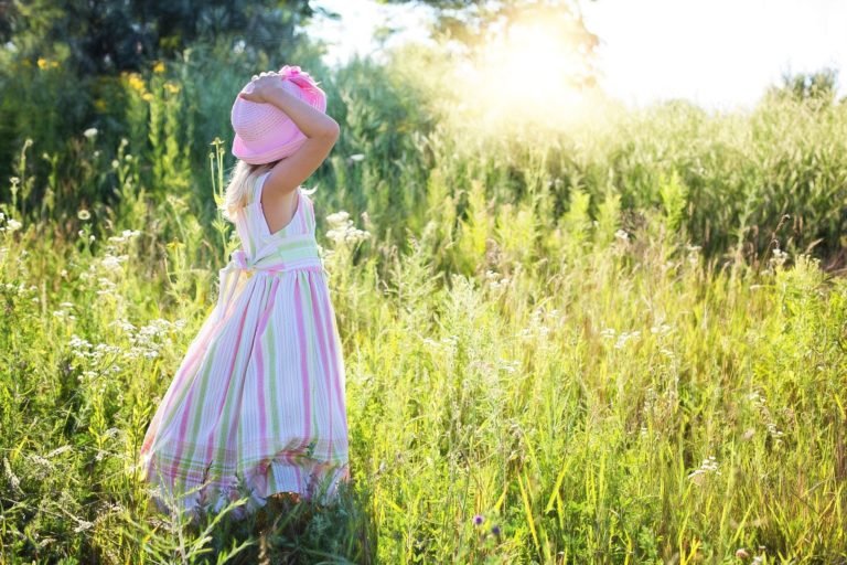 Niña en el campo sujetando su sombrero